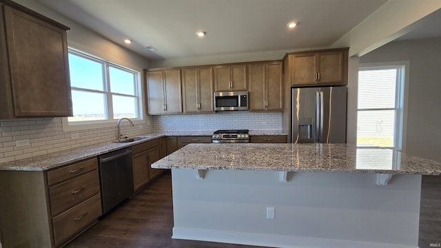 kitchen featuring dark wood-style flooring, a sink, decorative backsplash, appliances with stainless steel finishes, and a kitchen breakfast bar