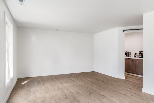 spare room featuring a barn door, visible vents, light wood-style flooring, and baseboards