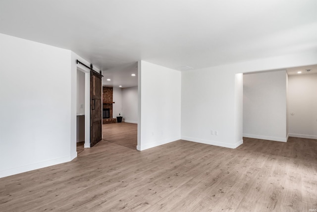 spare room featuring a barn door, baseboards, wood finished floors, a brick fireplace, and recessed lighting