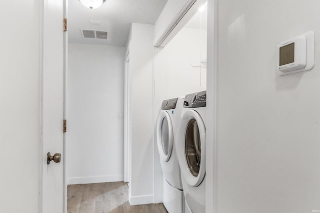 clothes washing area with a textured ceiling, laundry area, visible vents, washer and dryer, and light wood finished floors