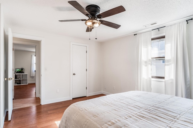 bedroom with visible vents, ceiling fan, a textured ceiling, wood finished floors, and baseboards