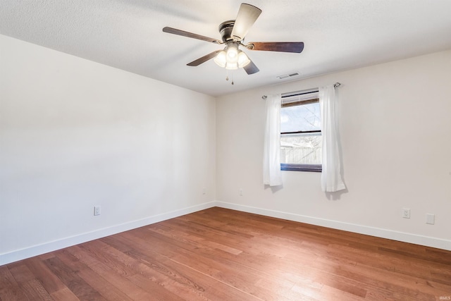 spare room featuring a ceiling fan, visible vents, baseboards, and wood finished floors