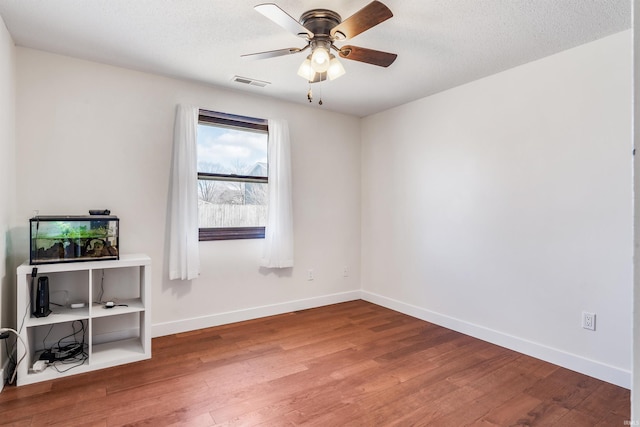 spare room featuring a ceiling fan, baseboards, visible vents, and wood finished floors