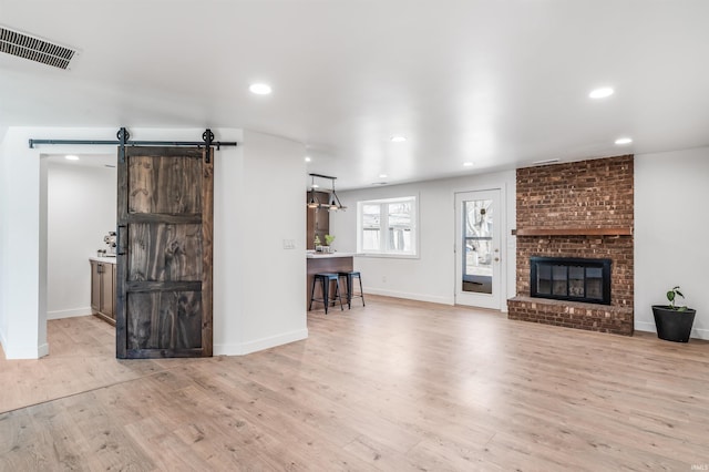 living area with a barn door, recessed lighting, a fireplace, wood finished floors, and visible vents