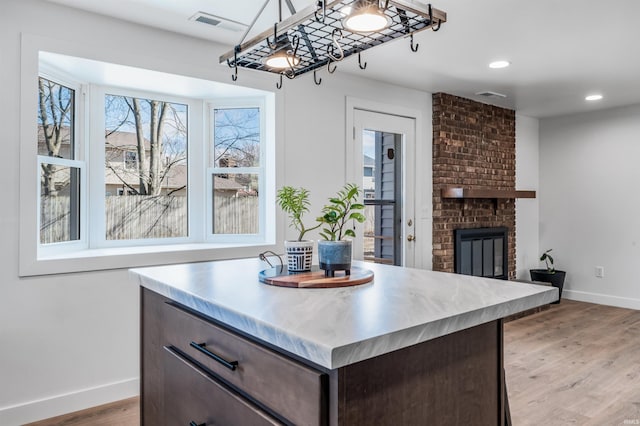 kitchen featuring a brick fireplace, baseboards, light wood-style flooring, and dark brown cabinets