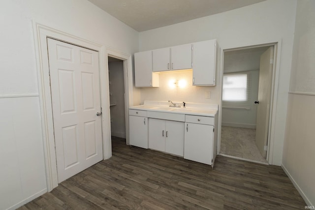 kitchen with dark wood-style floors, light countertops, white cabinetry, a sink, and baseboards