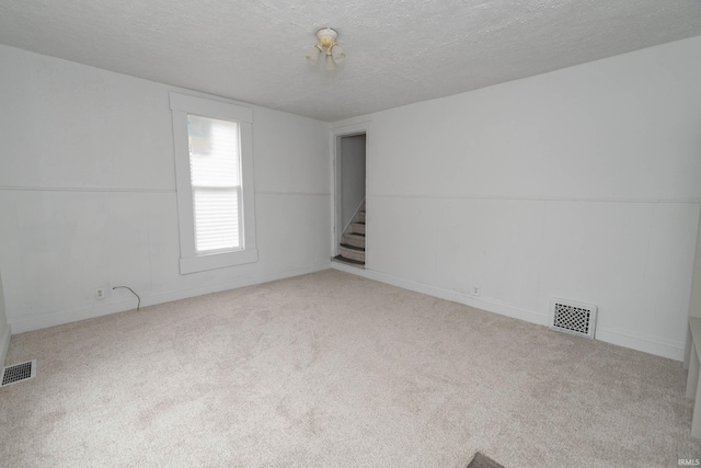 unfurnished room featuring carpet floors, visible vents, a textured ceiling, and stairs