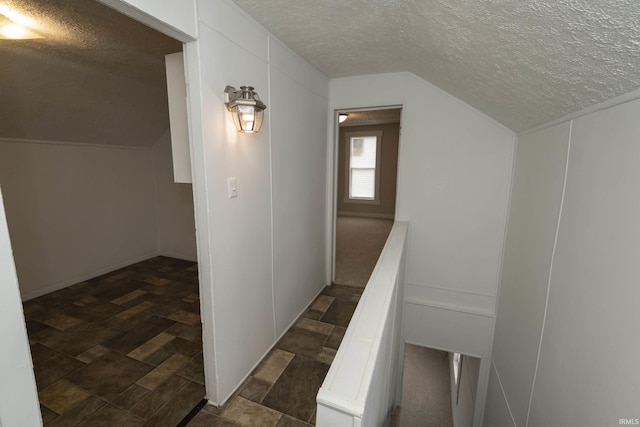 hall with stone finish flooring, vaulted ceiling, and a textured ceiling