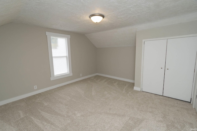 additional living space featuring lofted ceiling, light carpet, a textured ceiling, and baseboards