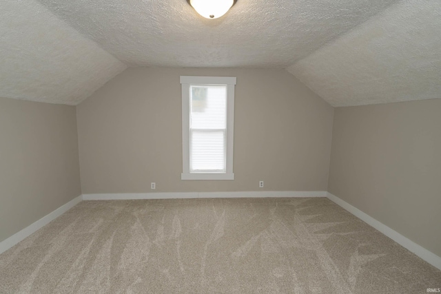 additional living space with carpet flooring, vaulted ceiling, a textured ceiling, and baseboards