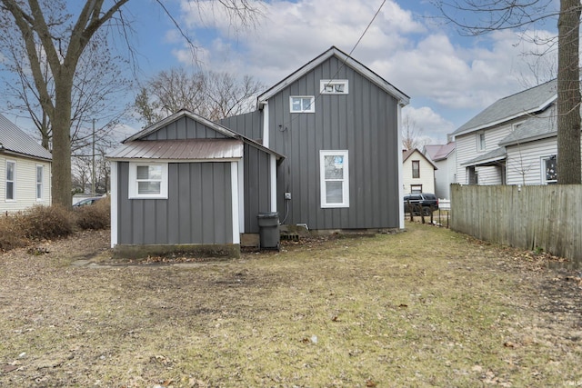 rear view of house featuring board and batten siding, metal roof, and fence