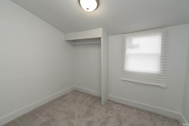 unfurnished bedroom featuring baseboards, a closet, and light colored carpet