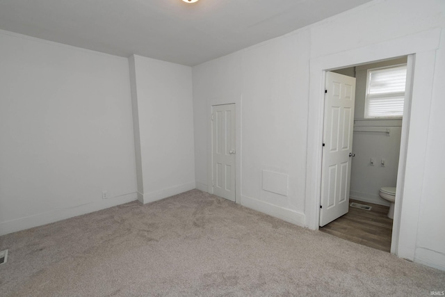 unfurnished bedroom featuring ensuite bathroom, carpet floors, and visible vents