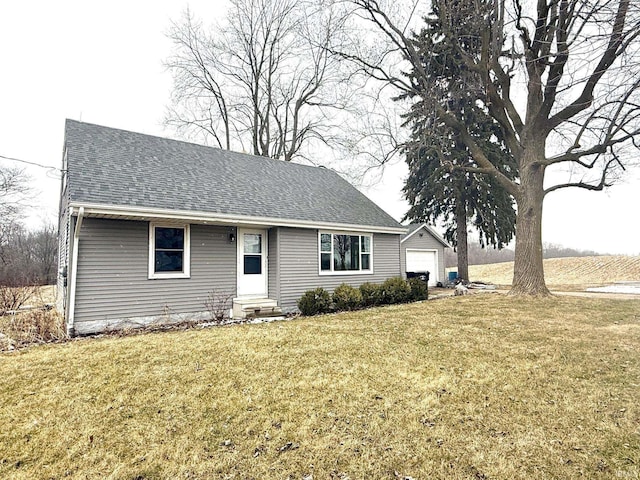 view of front facade with entry steps, roof with shingles, a detached garage, and a front yard