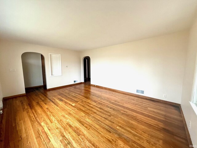 unfurnished room featuring arched walkways, baseboards, visible vents, and light wood finished floors