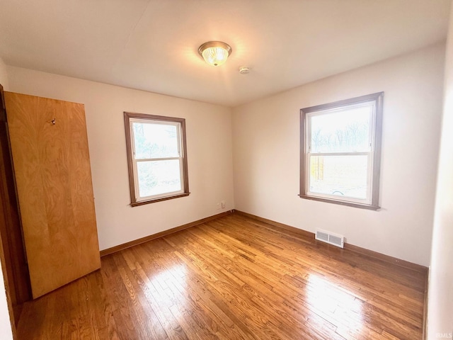 empty room with baseboards, visible vents, and light wood finished floors