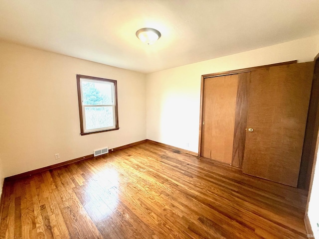 unfurnished bedroom featuring a closet, visible vents, baseboards, and wood finished floors