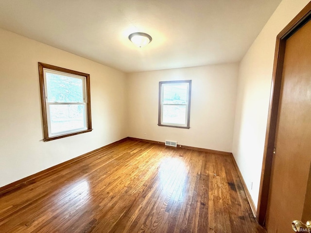 spare room featuring hardwood / wood-style flooring, baseboards, visible vents, and a wealth of natural light