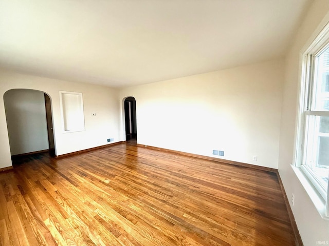 empty room featuring baseboards, visible vents, arched walkways, and wood finished floors