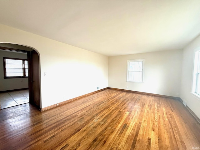 unfurnished room featuring arched walkways, hardwood / wood-style floors, and plenty of natural light