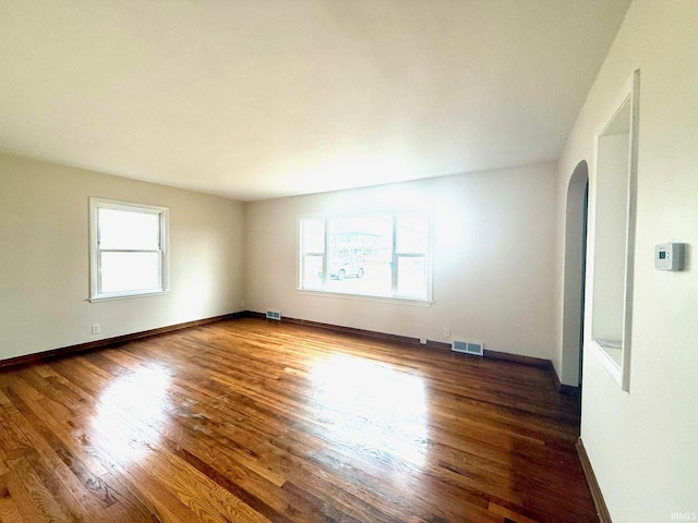 spare room featuring arched walkways, visible vents, baseboards, and wood finished floors