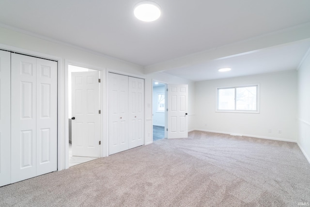 unfurnished bedroom featuring multiple closets, carpet flooring, crown molding, and baseboards