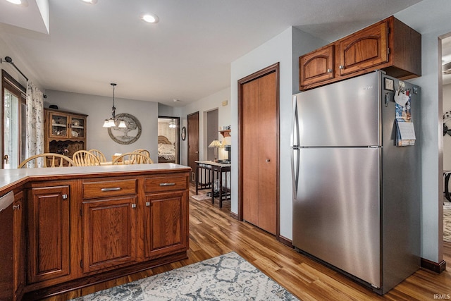 kitchen featuring dishwashing machine, light wood-style flooring, freestanding refrigerator, brown cabinetry, and decorative light fixtures