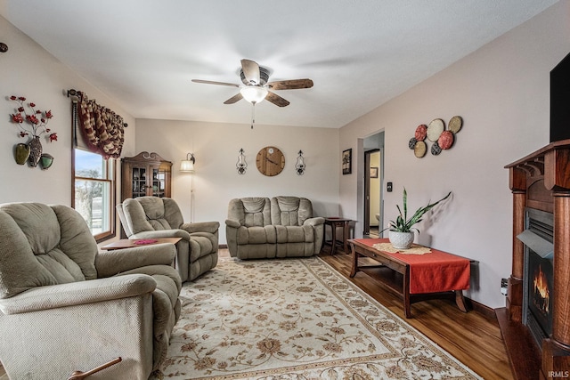 living area with a warm lit fireplace, ceiling fan, and light wood-style flooring