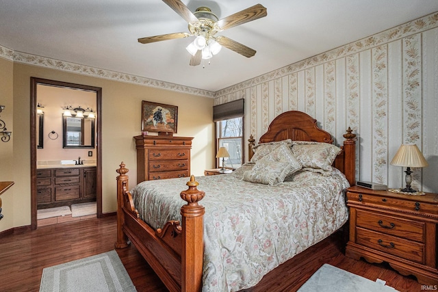 bedroom with wood finished floors, a ceiling fan, baseboards, ensuite bath, and wallpapered walls