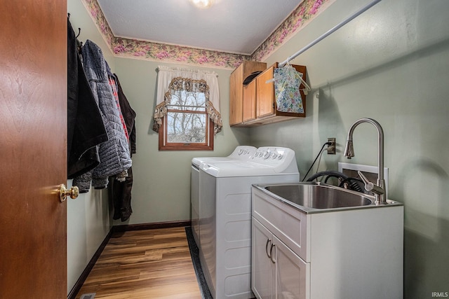 laundry area featuring cabinet space, baseboards, wood finished floors, washer and dryer, and a sink