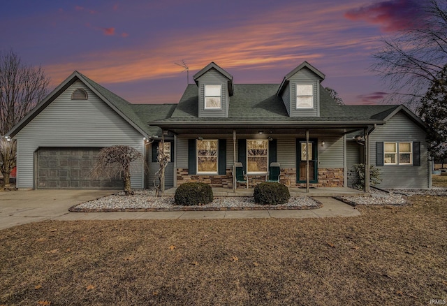 view of front facade with an attached garage, covered porch, concrete driveway, stone siding, and roof with shingles