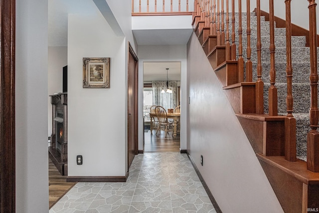 foyer entrance featuring a lit fireplace, stone finish flooring, stairs, and baseboards