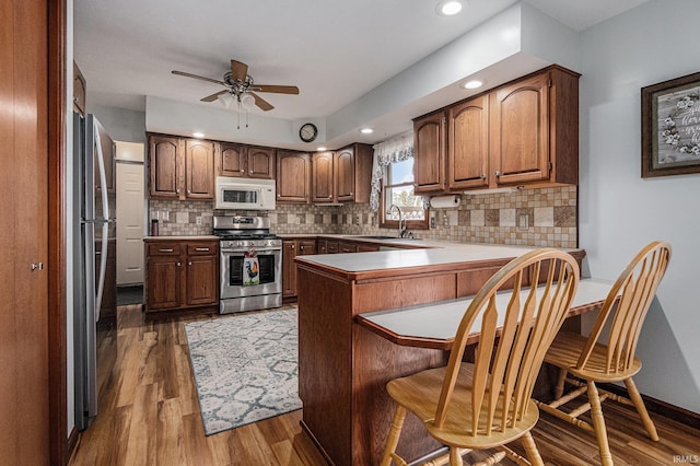 kitchen with tasteful backsplash, wood finished floors, a peninsula, stainless steel appliances, and a sink