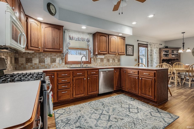 kitchen with light wood finished floors, stainless steel appliances, brown cabinetry, a sink, and a peninsula