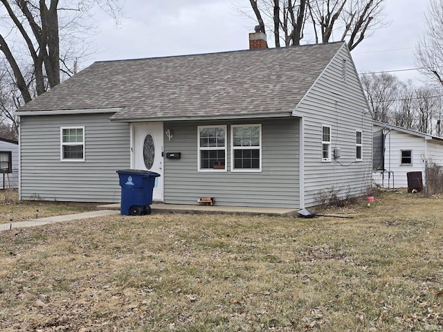 view of front of property with a front yard, roof with shingles, and a chimney