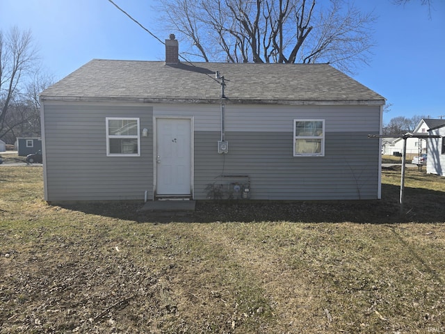 back of house featuring a lawn, roof with shingles, and a chimney