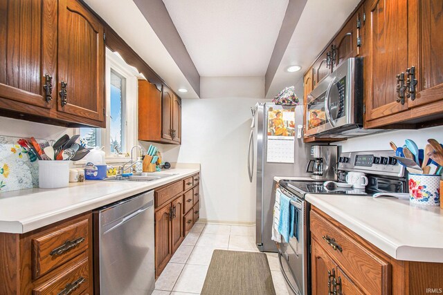 kitchen featuring brown cabinetry, stainless steel appliances, a sink, and light tile patterned flooring