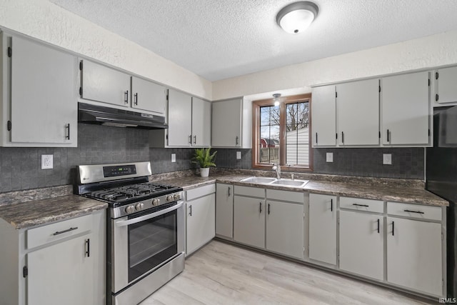 kitchen featuring dark countertops, under cabinet range hood, stainless steel range with gas cooktop, and a sink