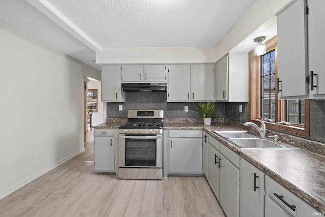 kitchen featuring stainless steel gas range oven, under cabinet range hood, a sink, light wood-style floors, and decorative backsplash