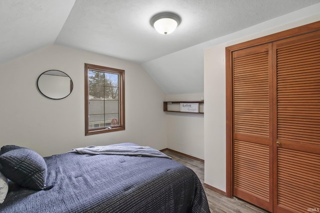 bedroom featuring baseboards, vaulted ceiling, a closet, and wood finished floors