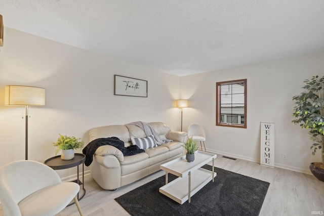 living room with light wood-type flooring, visible vents, and baseboards