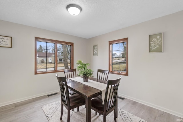 dining space with a textured ceiling, light wood-style flooring, visible vents, and baseboards