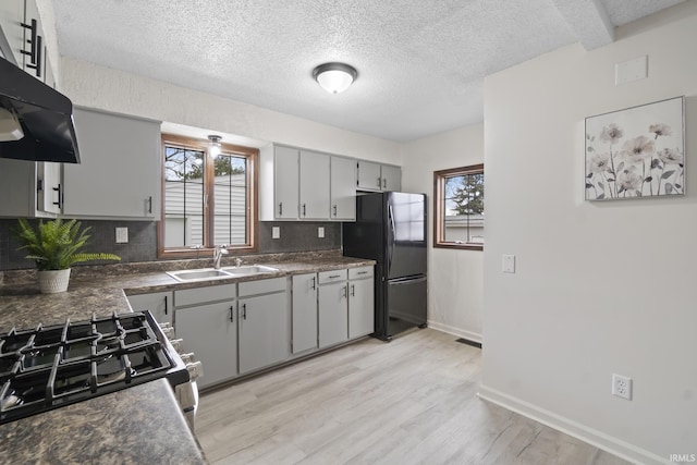 kitchen featuring dark countertops, exhaust hood, a sink, and freestanding refrigerator