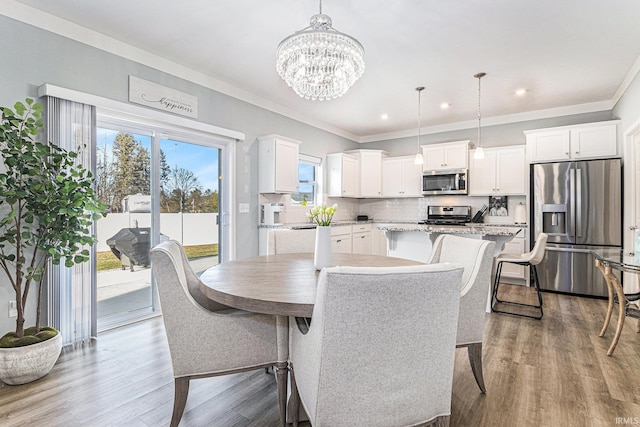 dining area with an inviting chandelier, crown molding, wood finished floors, and recessed lighting