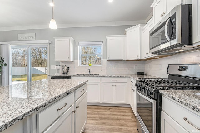 kitchen with light wood finished floors, stainless steel appliances, tasteful backsplash, white cabinetry, and a sink