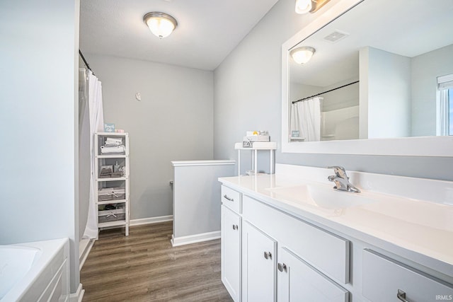 full bath featuring wood finished floors, vanity, visible vents, baseboards, and a tub