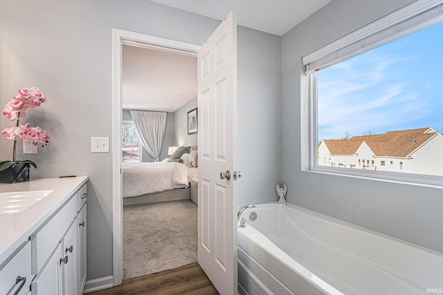 ensuite bathroom with vanity, wood finished floors, connected bathroom, and a bath