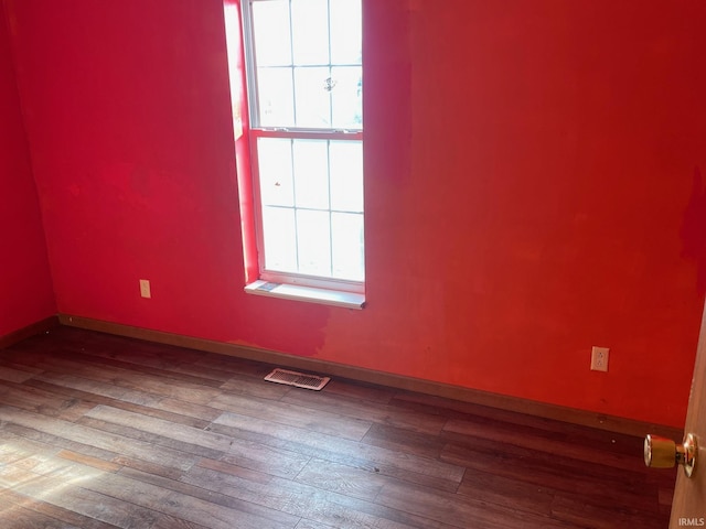 empty room with wood-type flooring, visible vents, and baseboards
