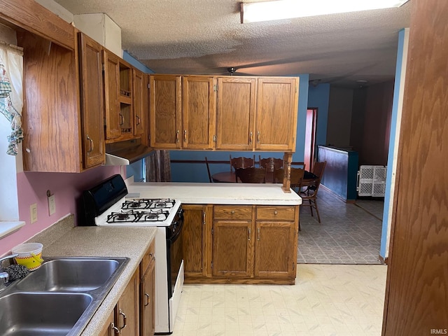 kitchen featuring brown cabinets, light floors, a sink, gas range, and under cabinet range hood