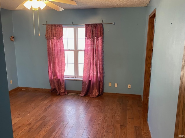 empty room featuring a textured ceiling, ceiling fan, wood-type flooring, and baseboards